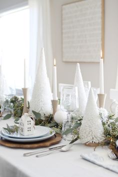 a dining room table decorated for christmas with white trees and greenery on the place setting