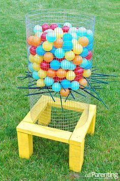 a bunch of balls that are in a cage on the grass near a table and chair