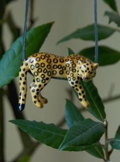 a yellow and black leopard ornament hanging from a tree branch with green leaves