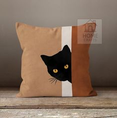 a black cat is peeking out from behind a brown pillow on a wooden table with a house in the background