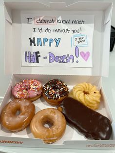 a box filled with donuts sitting on top of a white counter next to a sign that says i don't know what happy half dozen