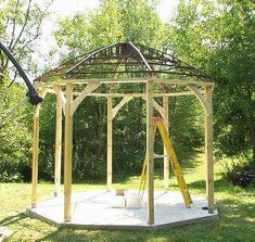 a wooden gazebo sitting on top of a lush green field next to a forest