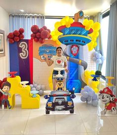 a man standing in front of a birthday decoration with cars and balloons on the floor