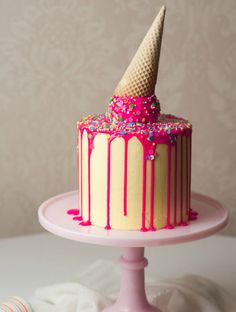 a cake with pink icing, sprinkles and an ice cream cone on top