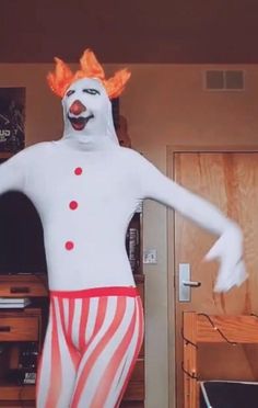 a man dressed as a clown standing in front of a tv screen and holding his arms out