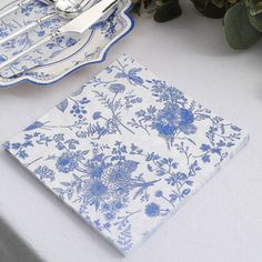 a blue and white table cloth with flowers on it next to silver utensils