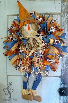 a scarecrow door hanger on the side of a white door with blue, orange and brown decorations