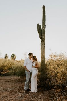 a pregnant couple standing in front of a saguado with their arms around each other