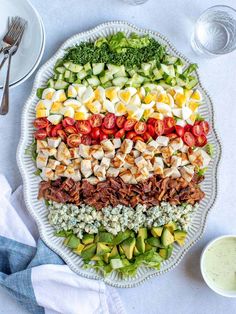 a large platter filled with meat, veggies and dressings on top of a white table