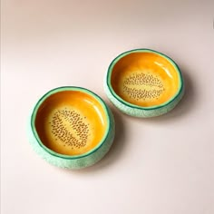 two yellow and green bowls sitting on top of a white table next to each other