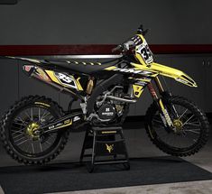 a yellow and black dirt bike sitting on top of a stand in front of a wall