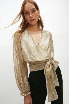 Illuminate the dancefloor in this metallic wrap top. A draped wrap design, this printed blouse will match the disco ball with its mesmerising finish. Shaped with a V-neckline and secured with a waist tie for a fit-and-flare silhouette, it has long sleeves and gathered cuffs. Add oversized hoops and pleated flares for some disco drama.Style: BlouseDesign: MetallicFabric: Fancy FabricLength: RegularNeckline: WrapSleeve Length: Long Sleeve Luxury Evening Blouse, Gold Tops Outfit, Formal Top, Gold Sequin Top, Evening Gala, Evening Blouses, Formal Tops, Gold Blouse, Evening Tops