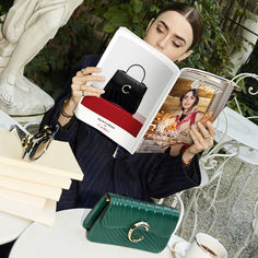 a woman sitting at a table holding up a book with an image of a purse on it