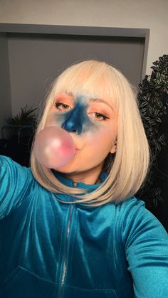 a woman with white hair and blue makeup blowing bubbles into her mouth while wearing a clown nose ring