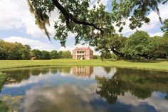 a large house sitting on top of a lush green field next to a lake in front of it