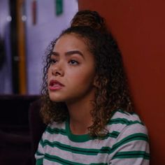 a woman sitting against a red wall in a room with other people standing behind her