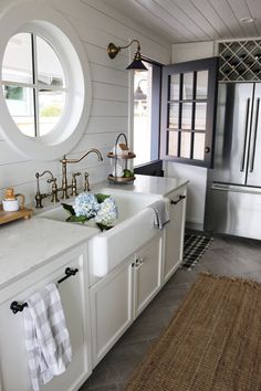 a white kitchen with two sinks and an oval window in the wall above it is also a rug on the floor