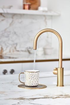 a golden faucet with a white coffee cup on it in front of a marble counter top