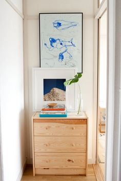 a wooden dresser topped with books next to a painting