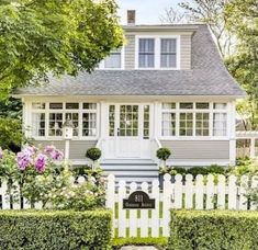 a white picket fence in front of a house with flowers and bushes around the perimeter