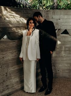 a man and woman standing next to each other in front of a wooden wall with palm trees