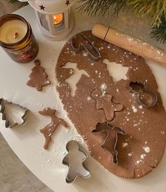 cookie cutters and cookies on a table next to a lit candle, christmas tree ornament