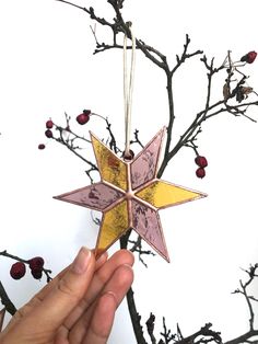 a hand holding an ornament in front of a tree