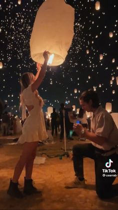 a woman holding up a paper lantern while another man sits on a bench in front of her