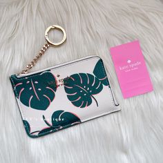 a white purse with green leaves on it next to a pink card holder and keychain