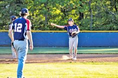 a baseball player throwing a ball to another player on the field with trees in the background