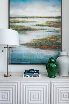 a green vase sitting on top of a white dresser next to a lamp and painting