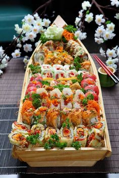 a long wooden boat filled with lots of sushi on top of a table next to flowers