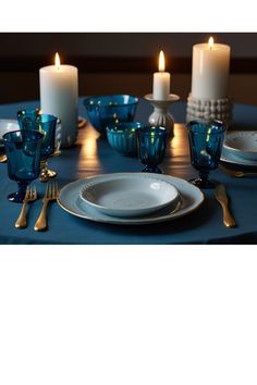 a table set with plates, candles and blue glassware is shown in this image