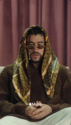 a man wearing glasses and a hoodie sitting on a couch with his arms crossed