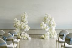 the chairs are lined up with white flowers on them and blue ribbons tied to them