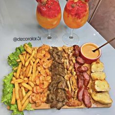 a platter filled with different types of food next to two glasses of juices