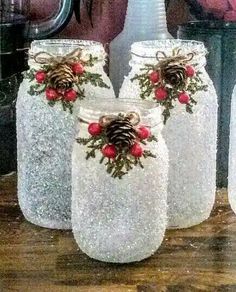 three mason jars decorated with pine cones and red berries