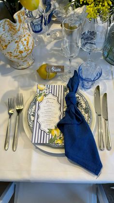 a white table topped with a plate and silverware next to a vase filled with yellow flowers