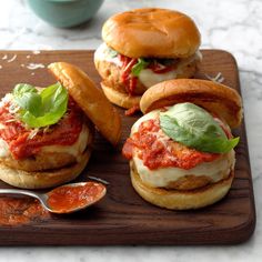 three mini sandwiches with sauce and cheese on a wooden tray next to dipping spoons