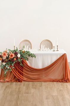 the table is set with an orange drape draped over it and flowers on top