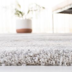 a close up view of a white carpet with a potted plant in the background