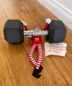 an elf is sitting on the floor with two dumbbells and a note that says help