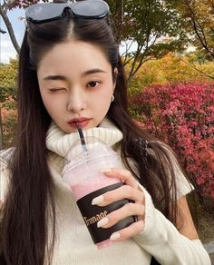 a woman with long hair and sunglasses holding a drink in front of her face while looking at the camera