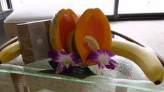 a banana and orange slices on a glass table with purple orchids in the foreground