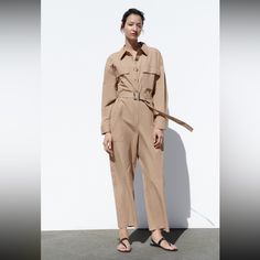 Long Sleeve Lapel Collar Jumpsuit. Front Patch Pockets. Tonal Belt With Buckle. Front Zip And Button Closure. Spring Workwear Pantsuit With Button Closure, Summer Pantsuit With Buttons, Chic Jumpsuits And Rompers With Button Closure For Fall, Chic Fall Jumpsuits And Rompers With Button Closure, Chic Jumpsuits And Rompers With Buttons For Fall, Summer Workwear Pantsuit With Buttons, Beige Jumpsuits And Rompers For Spring Daywear, Chic Spring Jumpsuits And Rompers With Button Closure, Chic Jumpsuits And Rompers With Buttons For Spring