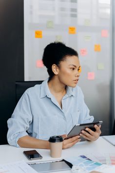 a woman sitting at a table with a tablet in front of her and papers on the wall behind her