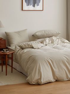 an unmade bed in a bedroom with a painting on the wall and wooden floor