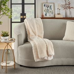 a couch with a blanket on it in front of a window and potted plant