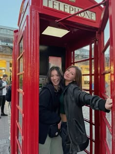 two women standing in a red phone booth