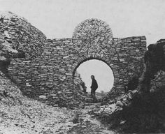 an old photo of a man and his dog standing in a stone wall with a circular window